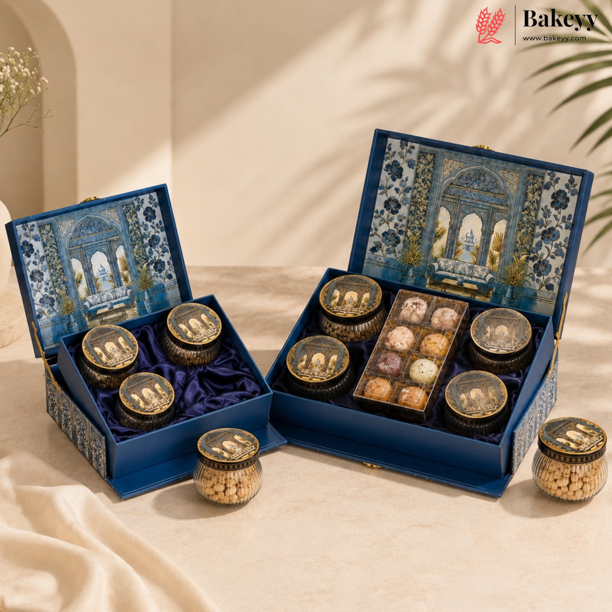 Two ornate blue gift boxes filled with assorted chocolates and nuts, displayed on a draped cream fabric with soft shadows. The boxes feature intricate blue and gold architectural patterns on the inside lids, and the brand name Bakew is visible in the top right corner.