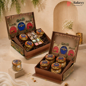 Two ornate Bakeyy gift boxes filled with assorted packaged snacks and jars, displayed on a warm beige set with decorative arches, hanging greenery, and small floral arrangements.