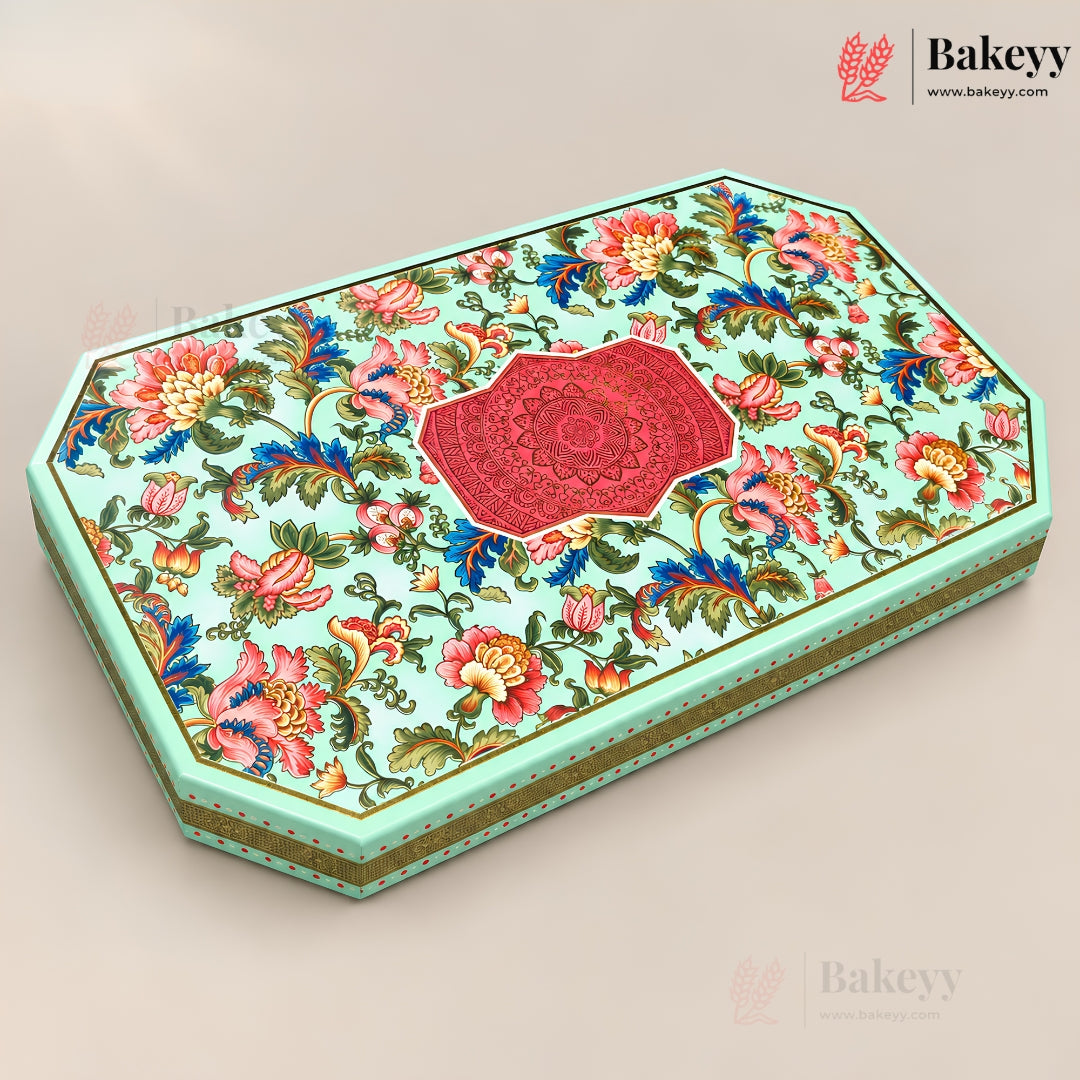 An octagonal decorative gift box with a light mint green base, covered in a colorful floral pattern with pink, red, blue, and yellow flowers, and a central red mandala design on the lid. The box is shown at an angle on a neutral beige background with Bakeyy branding in the corners.