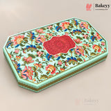 An octagonal decorative gift box with a light mint green base, covered in a colorful floral pattern with pink, red, blue, and yellow flowers, and a central red mandala design on the lid. The box is shown at an angle on a neutral beige background with Bakeyy branding in the corners.