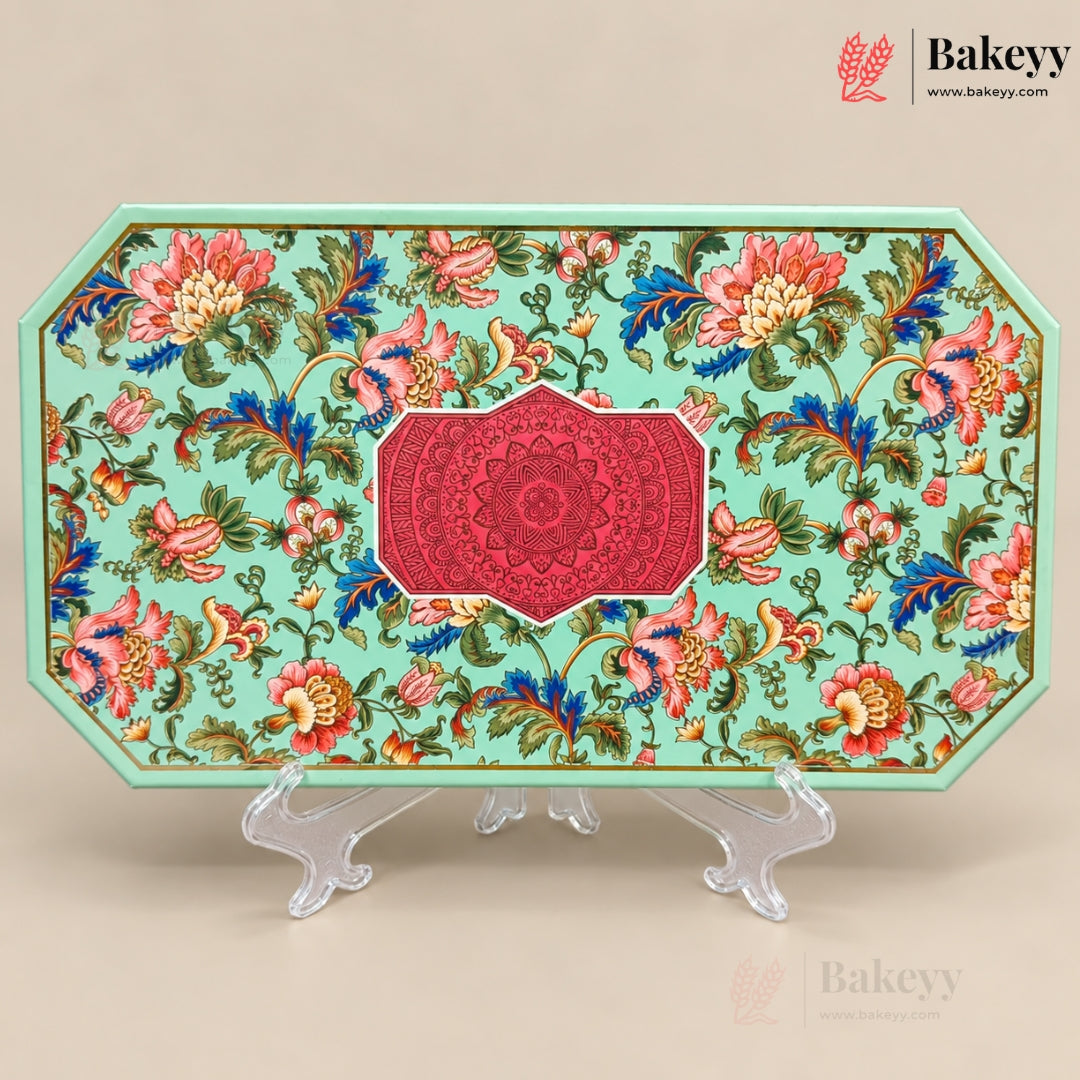 An octagonal decorative cake board or serving tray with a light mint green background, covered in a colorful floral pattern with pink, red, blue, and green elements, and a central red mandala design. It is displayed on clear acrylic stands against a solid beige background.