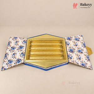 An open hexagonal bakery gift box with a gold interior tray and patterned blue-and-white flaps, photographed on a plain beige background. A Bakeyy logo watermark appears in the top right corner.