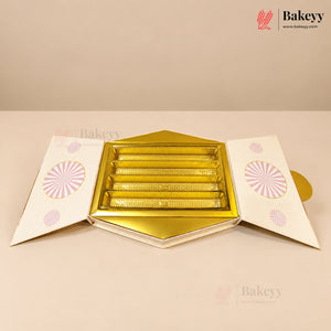 A hexagonal gold and white bakery gift box, shown open to reveal five individual rectangular slots inside. The flaps of the box are white with pink circular sunburst patterns.