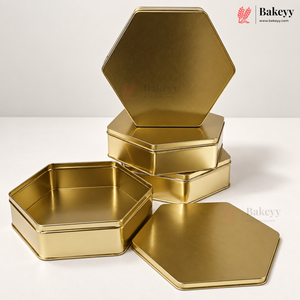 Five gold hexagonal metal tins, including one open tin and four stacked closed tins, displayed on a clean white surface against a light gray background. The Bakeyy brand logo is visible in the top right corner.
