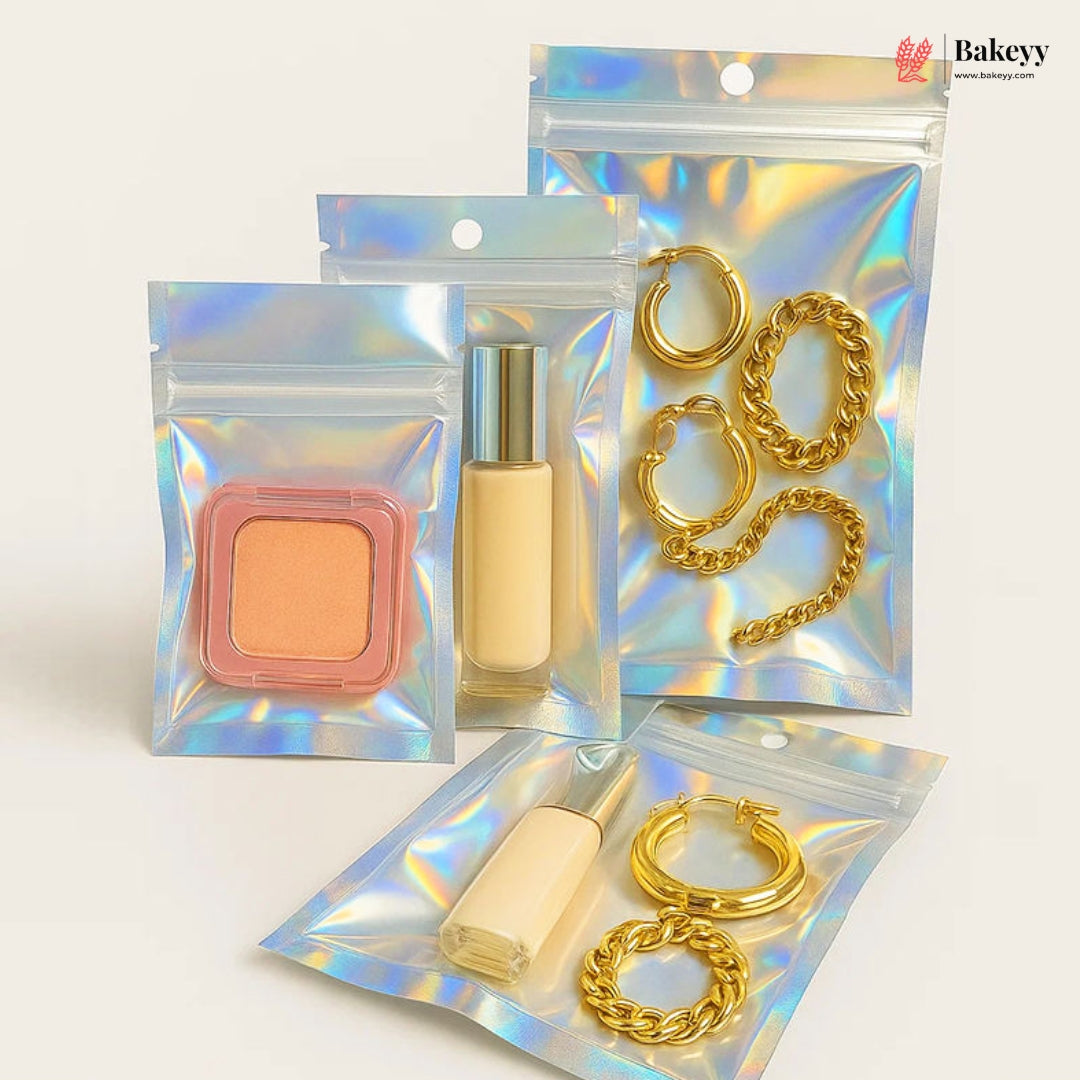 Four iridescent holographic zipper pouches arranged on a light beige background. Two pouches contain gold-tone chain and hoop earrings, and two contain cosmetic items: a peach-colored square compact and a beige liquid bottle with a silver cap.