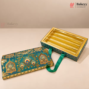An ornate rectangular gift box for chocolates, shown closed on the left and open on the right to reveal gold-trimmed compartments. The box features a teal and gold patterned fabric lid with a green ribbon handle, photographed on a neutral beige background.