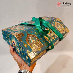 A hand holds a rectangular gift box wrapped in teal and gold patterned paper with a shiny green ribbon tied around it. The box has ornate gold arch motifs and decorative illustrations.