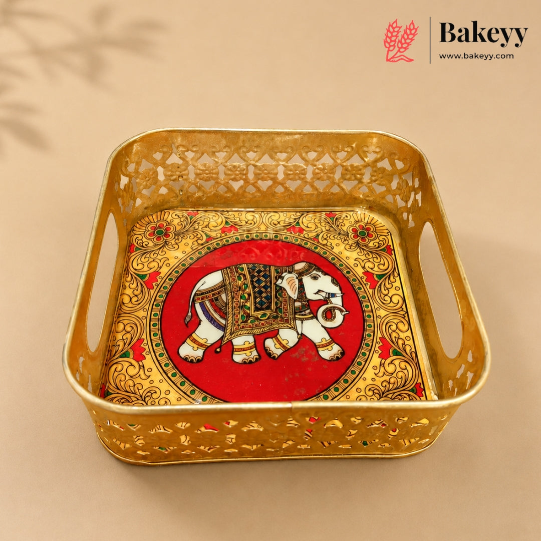 A square gold-colored metal tray with decorative cutouts and side handles, featuring an ornate red and gold elephant motif in the center. The Bakeyy brand logo is visible in the top right corner.