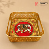 A square gold-colored metal tray with decorative cutouts and side handles, featuring an ornate red and gold elephant motif in the center. The Bakeyy brand logo is visible in the top right corner.