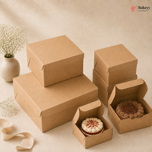 A set of brown kraft paper bakery boxes in various sizes, with two boxes shown open and holding decorated cakes, arranged on a beige background with a small vase of baby's breath.