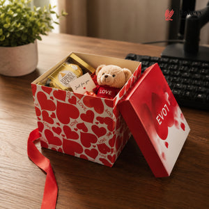 Open gift box with teddy bear and chocolates on a desk