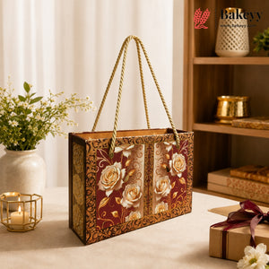A decorative gift box with rope handles, featuring a burgundy and gold floral pattern with cream roses, displayed on a table in a warm, styled interior setting.