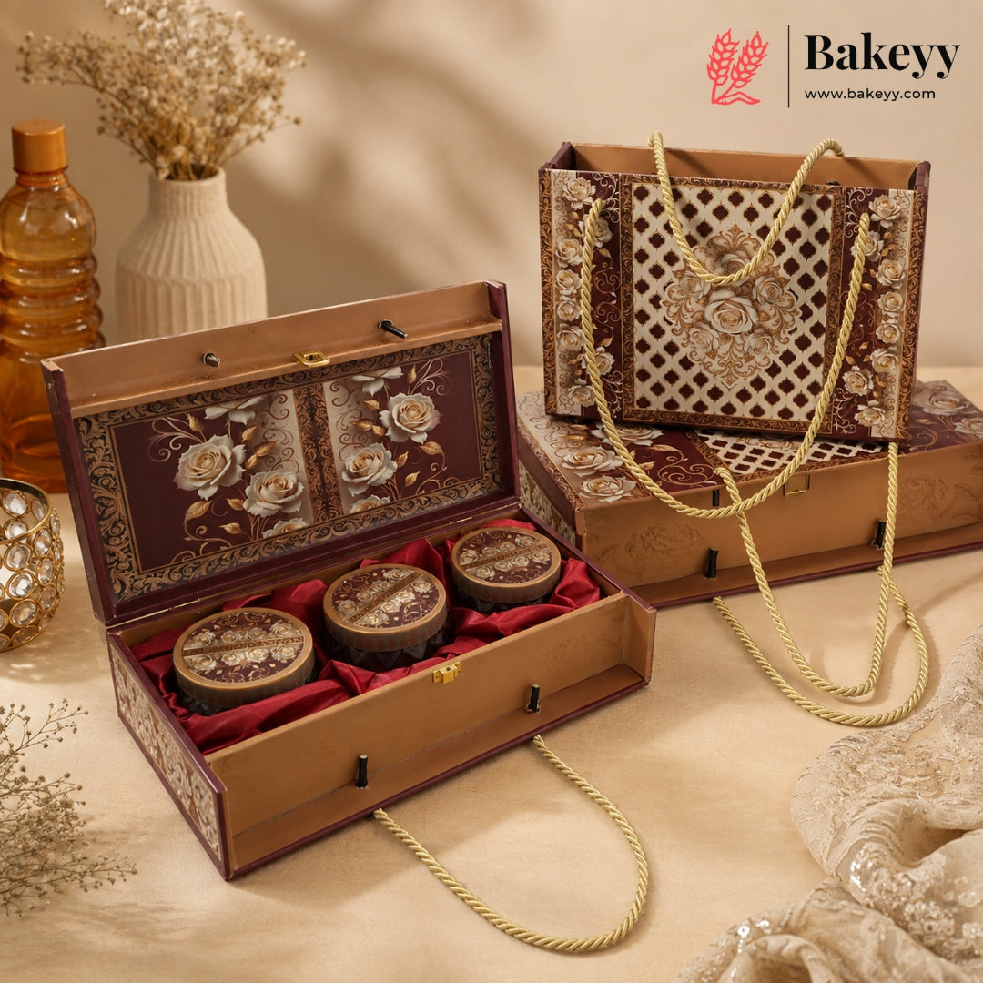 An ornate rectangular gift box set displayed on a beige fabric surface. The set includes an open box with three round decorative items inside, a matching closed box, and a decorative tote bag with rope handles.