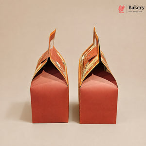 Two red paper gift boxes with orange printed handles, shown from the back on a plain beige background. A Bakeyy logo is visible in the top right corner.