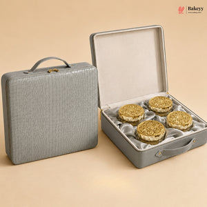 A gray textured hard case shown closed on the left and open on the right, containing four round gold-toned decorative items on a beige satin lining. The scene is photographed on a warm beige studio background with a Bakeyy watermark in the top right.