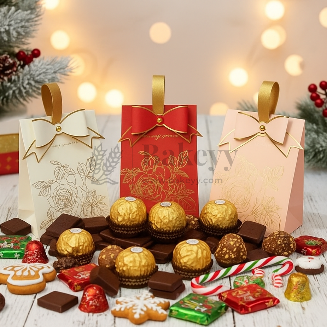 Assorted chocolates and candies on a wooden surface with decorative lights and Christmas trees in the background.