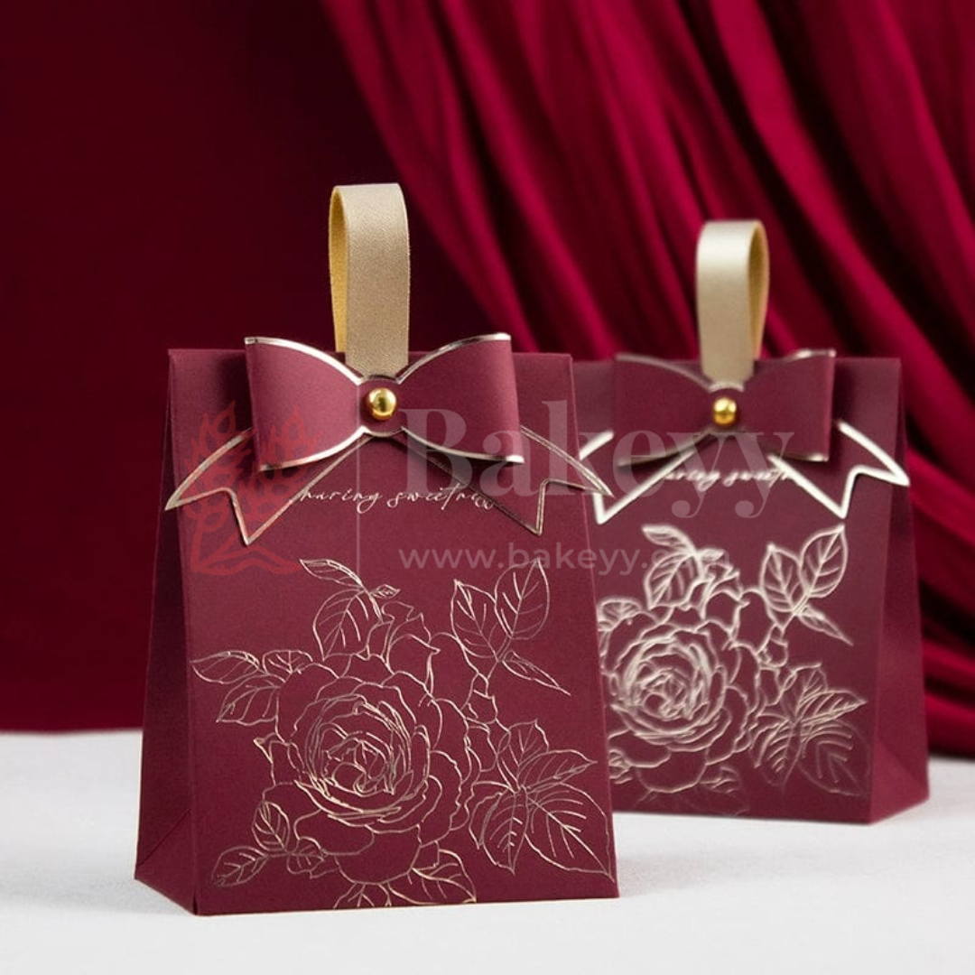 Two maroon gift bags with floral designs and gold ribbons on a red curtain background.