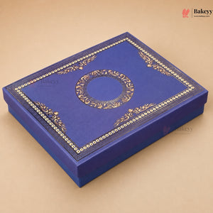 A royal blue rectangular gift box with ornate gold foil detailing, featuring a central circular medallion and decorative borders on the lid, set against a solid beige background.