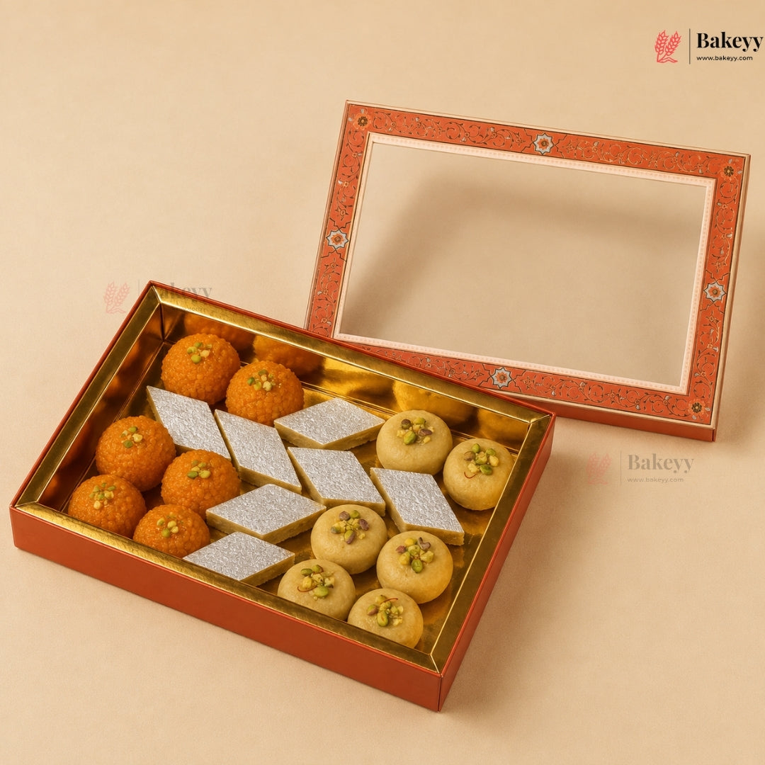 An open traditional Indian sweet gift box filled with orange marzipan laddos, beige pistachio-topped sweets, and silver-colored rectangular sweets, shown with the decorative lid propped behind on a warm beige background.