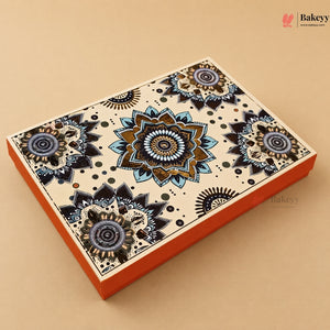 A rectangular decorative gift box with a cream-colored lid featuring intricate blue, black, and brown mandala patterns, with a bright orange base, shown on a solid beige background.
