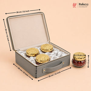 Gray rectangular gift box with a handle and satin lining, shown open with three round gold-covered items inside. Black dimension arrows and text label the box measurements, with a small jar shown beside it.