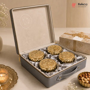 An open gray presentation box with a satin-lined interior holding four round golden-brown pastries, styled on a beige surface with decorative props and a branded Bakeyy logo in the top right.