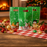 Three green Christmas gift bags with festive designs on a wooden table with holiday decorations.