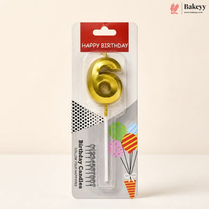 A gold metallic number 6 birthday candle in its original retail packaging, featuring a red 'HAPPY BIRTHDAY' header and festive balloon graphics on a light beige background.