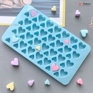A light blue silicone mold tray with multiple heart-shaped cavities, shown on a gray surface with small pastel heart-shaped pieces scattered around it.