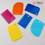 Six colorful plastic pastry scrapers in pink, orange, blue, yellow, and light blue, arranged on a light gray background with a Bakeyy logo in the top right corner.