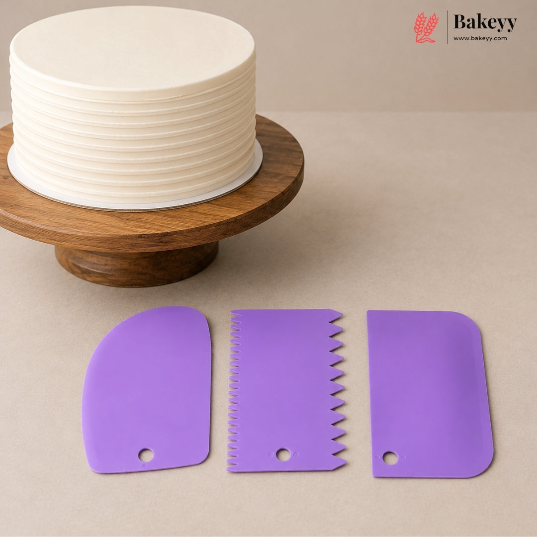 Three purple silicone cake scrapers displayed on a beige surface, with a partially decorated round cake on a wooden stand in the background. The Bakeey logo is visible in the top right corner.