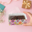 Hand holding a box of brownies with a decorative pattern on a pink background