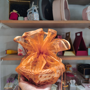 Woven basket with orange sheer ribbon held in front of a shelf with various items.