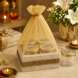Decorative box with jars and a sheer gold cover on a festive background with candles and flowers.