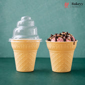 Two yellow waffle-cone-shaped dessert cups on a teal surface against a teal background. The left cup has a clear plastic tiered lid, and the right cup is filled with pink ice cream or gelato topped with chocolate drizzle and sprinkles.