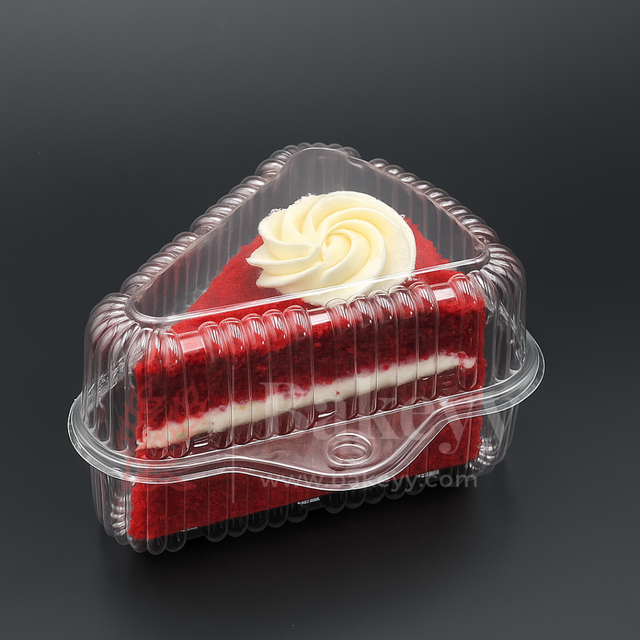 Slice of red velvet cake with white frosting in a clear plastic container on a black background