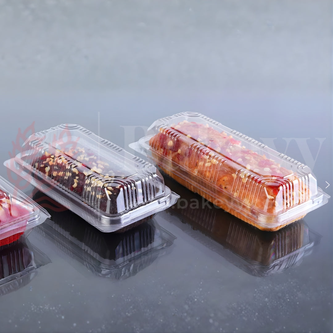 Three cake slices in clear plastic containers on a reflective surface with a blurred background.