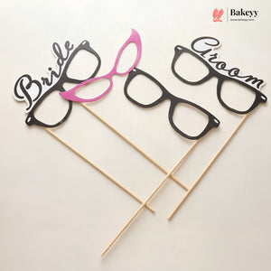 Glasses-shaped photo booth props labeled 'Bride' and 'Groom' on sticks with Bakeyy branding.