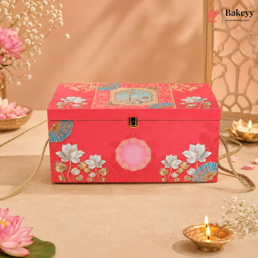 A rectangular red decorative jewelry box with floral and geometric patterns, featuring a gold clasp and a pink oval detail on the front, styled on a beige surface with flowers and candles.