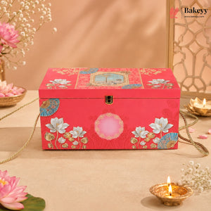 A rectangular red decorative jewelry box with floral and geometric patterns, featuring a gold clasp and a pink oval detail on the front, styled on a beige surface with flowers and candles.