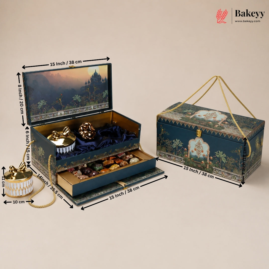 An ornate jewelry and confection gift box shown both closed and open, with dimension labels around it on a plain beige background. The closed view shows a dark blue illustrated exterior with gold rope handles; the open view reveals a gold interior, velvet lining, decorative pieces, and assorted chocolates or sweets in a tiered tray.