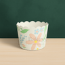 Floral design cupcake wrapper on a wooden surface with a green background