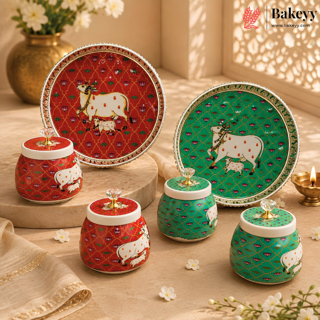 A set of decorative ceramic jars and plates with cow motifs, arranged on a beige surface with warm sunlight and shadows. The set includes red and green patterned plates and matching jars with white lids and gold-tone knobs.