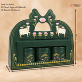 A dark green wooden tea gift box with decorative pink lotus and white cow motifs, shown with dimension lines indicating 32 cm width, 26 cm height, and 8 cm depth. The box contains three round tin boxes and is photographed on a beige background with text noting included paper bags and round tin boxes.