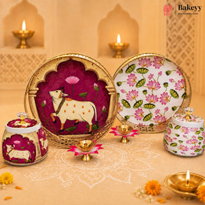 A set of decorative Indian-style ceramic plates and jars with floral and cow motifs, arranged on a beige patterned surface with lit diya candles and a warm architectural backdrop. The Bakeyy brand logo is visible in the top right corner.