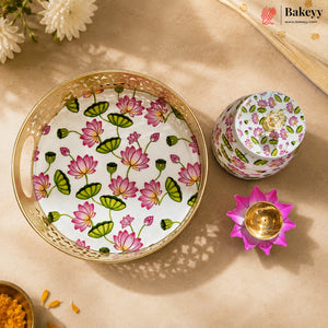 A decorative round tray and matching small container set with a pink and green lotus flower pattern on a white background, styled on a beige surface with a gold-toned flower-shaped candle holder and floral props.