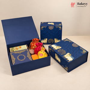 A luxury gift box set for baked goods, featuring a large navy blue box with gold patterns shown open to reveal assorted tea, sweets, and small drawstring pouches, alongside two closed matching boxes. The Bakeyy brand logo is visible in the top right corner.