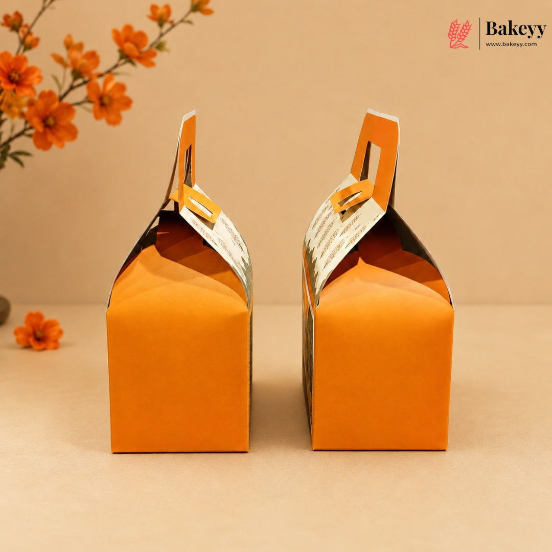 Two orange cardboard gift boxes with hinged handles, shown from the back on a beige surface against a beige background with orange flowers in the corner. A Bakeyy logo is visible in the top right.