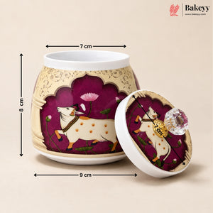 A decorative ceramic jar with its lid shown beside it, overlaid with dimension arrows and labels indicating 7 cm width, 8 cm height, and 9 cm lid diameter. The jar and lid are cream/beige with a deep purple panel featuring a white goat and pink floral motifs.