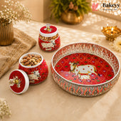 A set of red and white decorative ceramic containers and a matching serving tray with silver-toned embellishments, styled on a beige fabric surface with dried flowers, a brass pot, and a small brass lamp in the background.